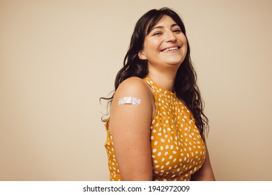 Beautiful Mature With Bandage On Her Arm After She Received Vaccination. Woman Smiling On Brown Background Feeling Happy To Get Inoculated.