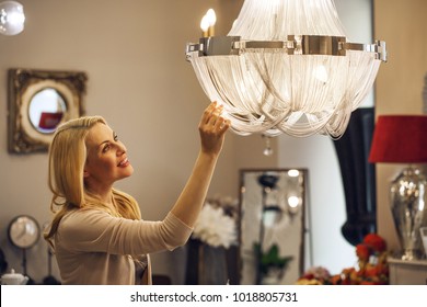 Beautiful mature blond haired woman checking out gorgeous crystal chandelier at the home decor store copyspace furniture supermarket coziness apartment shopping buying retail purchasing.