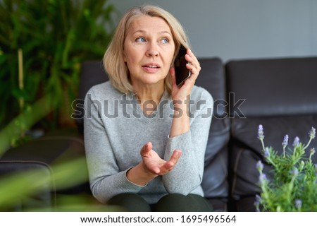 Beautiful mature blond woman talking on mobile phone at sofa
