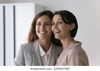 Beautiful mature Caucasian and young Hispanic businesswomen colleagues in elegant formal wear staring aside smiling posing indoors, feel happy, photoshoot for corporate album. Friendship at workplace - Powered by Shutterstock