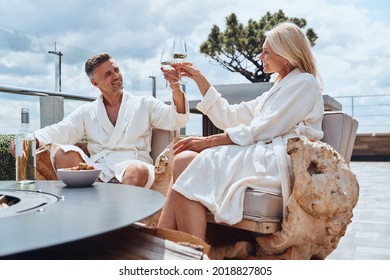 Beautiful mature couple in bathrobes enjoying fruits and wine while relaxing in luxury hotel outdoors
