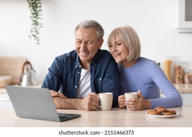 Beautiful mature couple enjoying time together at home, happy senior man and woman sitting at kitchen, drinking coffee with cookies and watching movie on laptop, copy space - Powered by Shutterstock