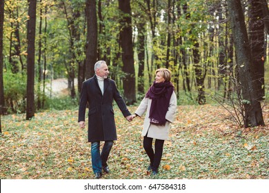 Beautiful Mature Couple Holding Hands And Walking In Autumn Park