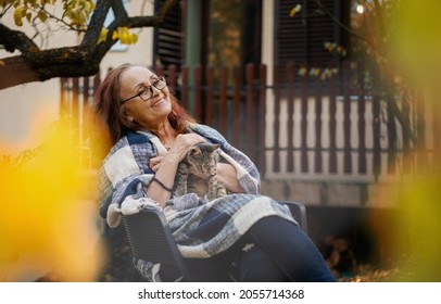 Beautiful mature happy smiling woman with a cat in her arms in the autumn garden of her country house