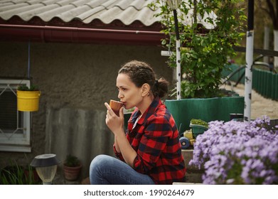 Beautiful Mature Hispanic Woman Gardener Drinking Hot Drink Resting Outside Country House. The Concept Of A Calm Outdoor Recreation Outside The City