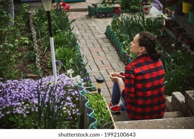 Beautiful Mature Hispanic Woman Gardener Resting Outside Country House. The Concept Of A Calm Outdoor Recreation Outside The City