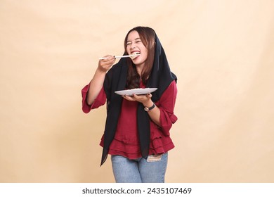 Beautiful mature indonesia woman in red shirt wearing a hijab bites dimsum with chopsticks cheerfully and carries a plate containing dimsum (Chinese food) candid. used for food and culinary content - Powered by Shutterstock