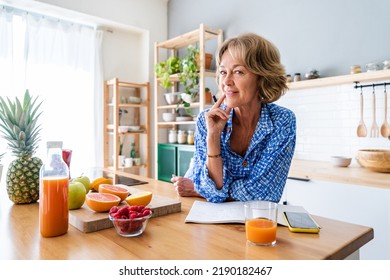 Beautiful mature senior woman at home, domestic life and leisure moments - 50-60 years old pretty female adult writing notes on the kitchen table - Shutterstock ID 2190182467