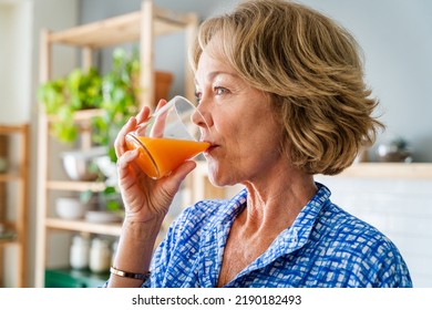 Beautiful mature senior woman at home, domestic life and leisure moments - 50-60 years old pretty female adult drinking healthy orange juice for breakfast - Powered by Shutterstock