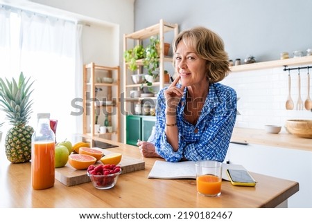 Beautiful mature senior woman at home, domestic life and leisure moments - 50-60 years old pretty female adult writing notes on the kitchen table