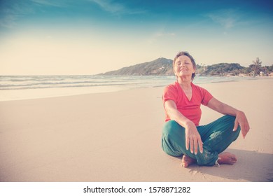 Beautiful Mature Woman 50 Years Old Resting In Lotus Position On The Beach By The Sea. Active Lifestyle, Travel And Sport For Senior Citizens.