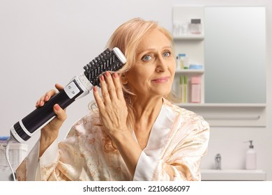 Beautiful Mature Woman In A Bathrobe Using A Hot Air Hair Brush Inside A Bathroom