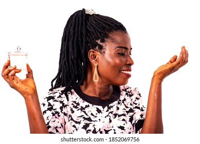 A Beautiful Mature Woman With Braids Standing On White Background Smelling Perfume On Her Arm Smiling.