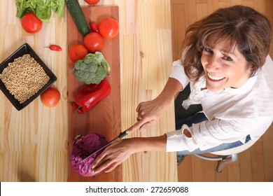 A Beautiful Mature Woman Cutting Vegetables In The Kitchen.