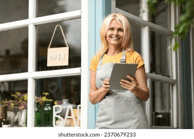 Beautiful Mature Woman With Digital Tablet Standing At Terrace Near Eco-Cafe, Happy Older Female Small Business Owner Using Modern Gadget And Smiling At Camera, Making Online Shopping - Powered by Shutterstock