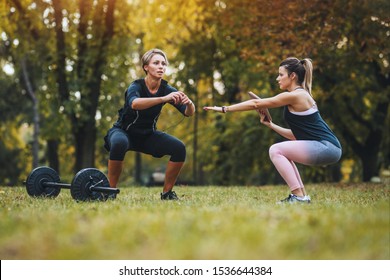 A beautiful mature woman is doing squat exercises with personal trainer in the park, dressed in a black suit with an EMS electronic simulator to stimulate her muscles. - Powered by Shutterstock