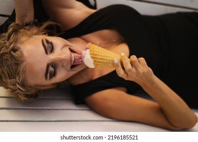 Beautiful Mature Woman Eating Ice Cream In A Waffle Cone While Lying On A Park Bench.