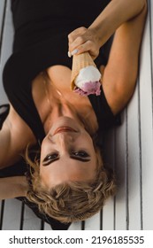 Beautiful Mature Woman Eating Ice Cream In A Waffle Cone While Lying On A Park Bench.