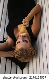 Beautiful Mature Woman Eating Ice Cream In A Waffle Cone While Lying On A Park Bench.