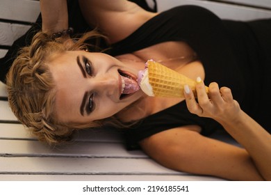 Beautiful Mature Woman Eating Ice Cream In A Waffle Cone While Lying On A Park Bench.