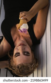 Beautiful Mature Woman Eating Ice Cream In A Waffle Cone While Lying On A Park Bench.