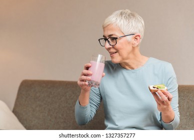 Beautiful mature woman full of energy drinking healthy fruit smoothie and holding toast with avocado, Healthy nutritious breakfast concept - Powered by Shutterstock