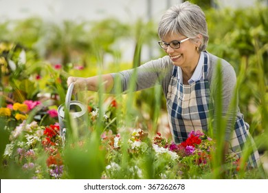 Beautiful Mature Woman In A Garden Watering Flowers