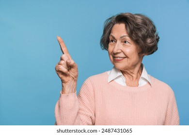 Beautiful mature woman grandmother in pink sweater looking at empty space while pointing at copy space isolated over blue background. Senior Caucasian granny showing free ad space - Powered by Shutterstock