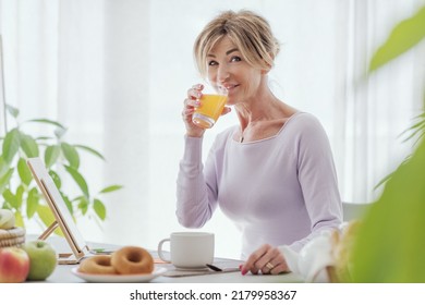 Beautiful Mature Woman Having A Relaxing Breakfast At Home, She Is Drinking Fresh Orange Juice