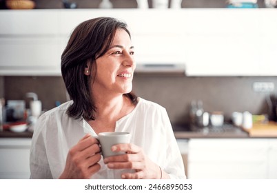 Beautiful mature woman in kitchen, drinking coffee. Older woman living alone, enjoying peaceful weekend day - Powered by Shutterstock