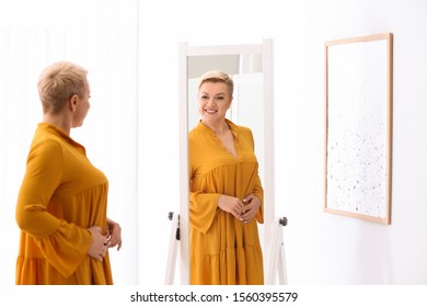 Beautiful Mature Woman Looking At Herself In Large Mirror Indoors