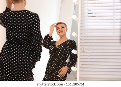 Beautiful Mature Woman Looking At Herself In Large Mirror With Lights Indoors