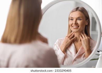 Beautiful Mature Woman Looking At Mirror And Touching Her Soft Skin On Neck, Attractive Middle Aged Female Smiling To Reflection, Enjoying Anti-Aging Skincare Routine At Home, Selective Focus - Powered by Shutterstock