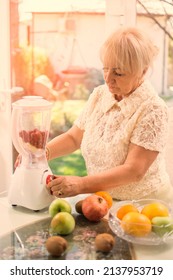 Beautiful Mature Woman Making Fruits Smoothies With Blender. Healthy Eating Lifestyle Concept. Senior Woman Preparing Drink With Bananas, Apple, Raspberries, Kiwi, Grapefruit And Orange At Home.