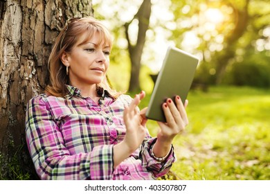 Beautiful mature woman in the park using a digital tablet