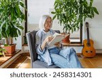 Beautiful mature woman reading book, feeling cozy and happy. Weekend activity for older woman, relaxing at home.