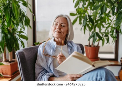 Beautiful mature woman reading book, feeling cozy and happy. Weekend activity for older woman, relaxing at home. - Powered by Shutterstock