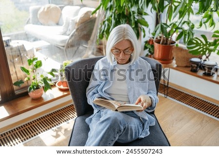 Beautiful mature woman reading book, feeling cozy and happy. Weekend activity for older woman, relaxing at home.