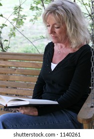 A Beautiful Mature Woman Relaxing And Reading On Her Porch Swing.