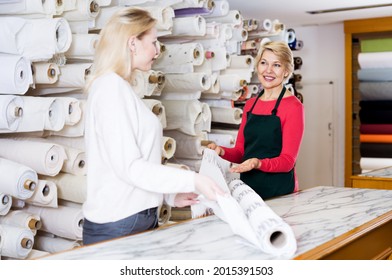 Beautiful Mature Woman Seller Displaying Diverse Fabrics To Young Customer In Textile Shop