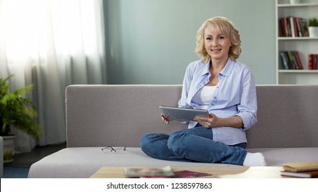 Beautiful mature woman sitting on couch and shopping online, looking into camera