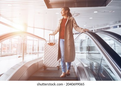 Beautiful Mature Woman Smiling And Looking Away While Moving By Escalator In Airport Terminal