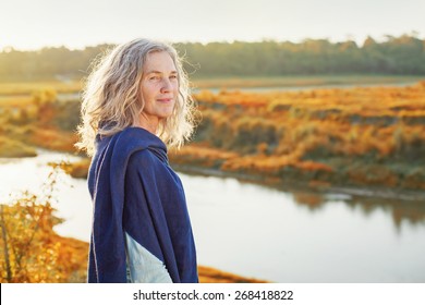 Beautiful mature woman standing in front of the river in autumn