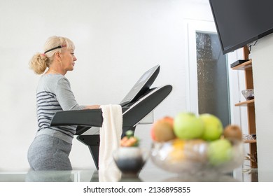 Beautiful Mature Woman Walking On Treadmill And Watching TV In The Living Room At Home