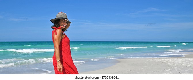 Beautiful Mature Woman Wearing a Red Summer Dress on the Beach