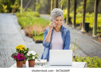 Beautiful Mature Woman Working In A Greenhouse And Making A Phone Call