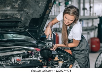 Beautiful Mechanic  girl in a black jumpsuit and a white T-shirt changes the oil in a black car - Powered by Shutterstock