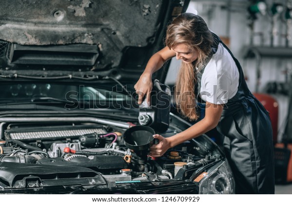 Beautiful Mechanic\
 girl in a black jumpsuit and a white T-shirt changes the oil in a\
black car. car repair\
concept
