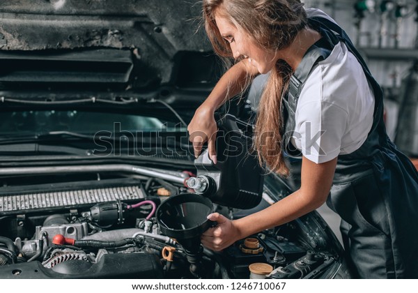 Beautiful Mechanic\
 girl in a black jumpsuit and a white T-shirt changes the oil in a\
black car. car repair\
concept