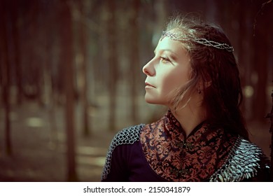 A beautiful medieval queen stands in a dense forest with a sunbeam falling on her face. Ancient legends. Fantasy world.